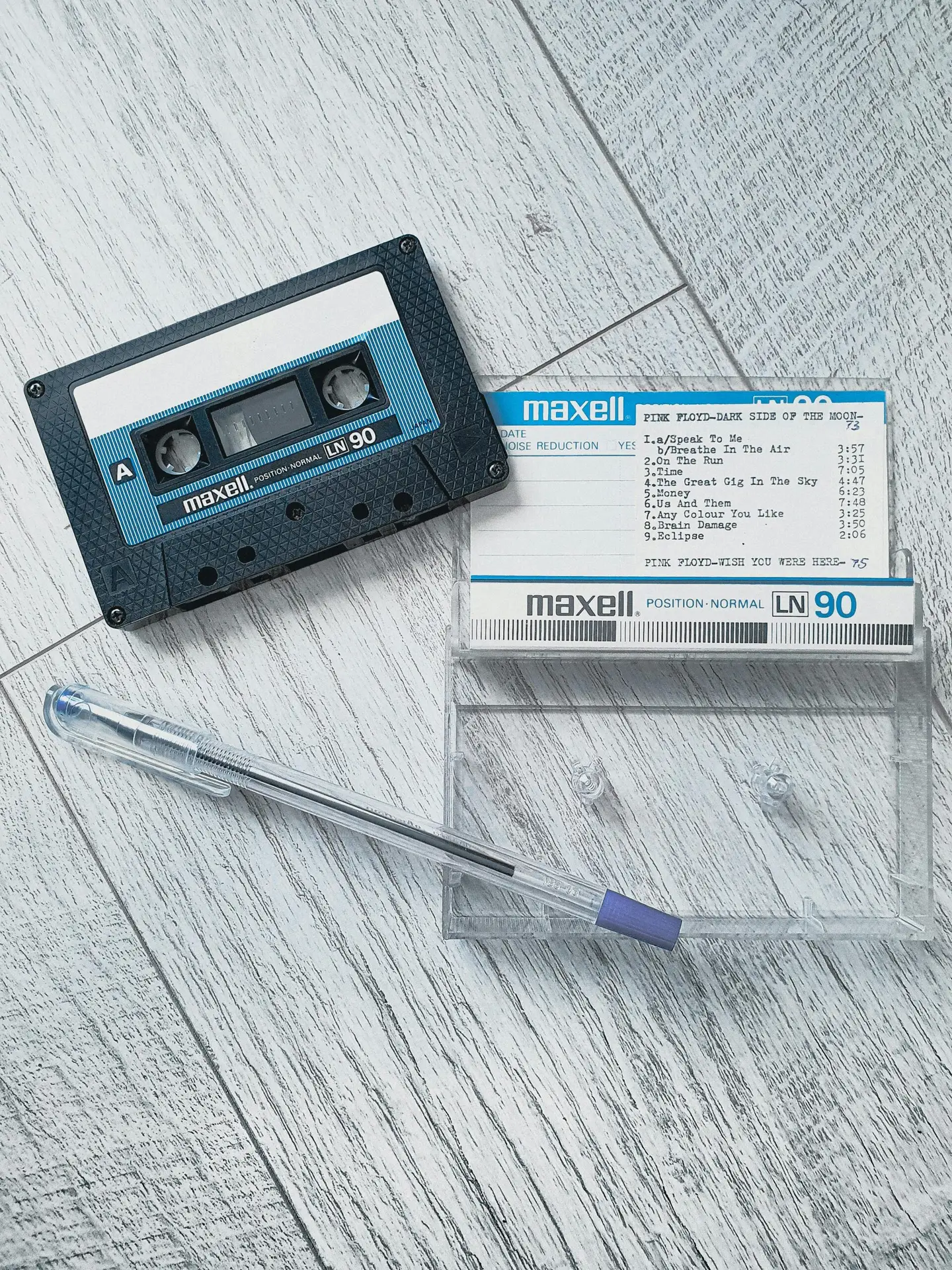 A nostalgic image of a vintage cassette tape, pen, and plastic case arranged on a wooden surface.